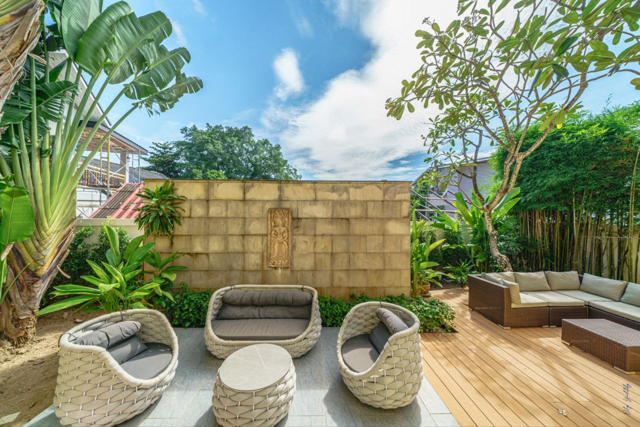 Sunny outdoor terrace with wicker furniture and tropical garden at The Himmaphan Phuket villa.